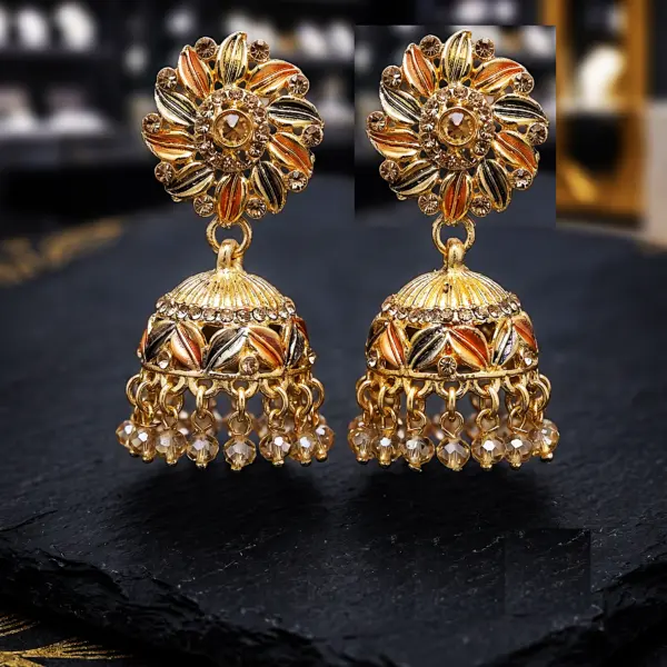 Gold plated floral jhumka earrings with enamel leaves and crystal bead drops on black stone surface